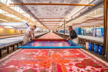 Deux artisans de Beauvillé à l'œuvre, imprimant à la main un motif au cadre plat sur une table d'impression textile, illustrant un savoir-faire traditionnel et minutieux.