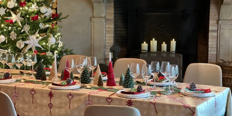 Nappe de Noël dressée dans la tradition des fêtes avec une allée centrale de bougies et figurines de sapins. Et un sapin en fond ainsi qu'une cheminée.