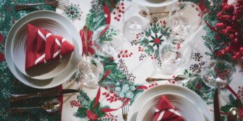 Focus sur la nappe Réveillon dressée avec une courronne de houx et des serviettes rouge pliée en forme de sapin.