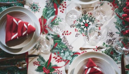 Focus sur la nappe Réveillon dressée avec une courronne de houx et des serviettes rouge pliée en forme de sapin.