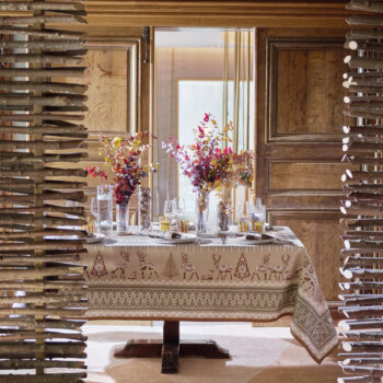 Table dressée avec la nappe Balade en Hiver coloris châtaigne, entourée de bois brut pour une atmosphère chalet et nature. Des feuilles d’eucalyptus séchées orangées et des noix décorent la table. En arrière-plan, une lumière automnale douce éclaire la scène, créant une ambiance chaleureuse et conviviale.