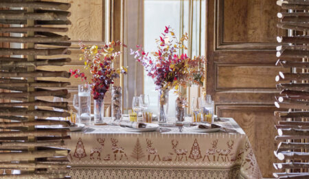 Table dressée avec la nappe Balade en Hiver coloris châtaigne, entourée de bois brut pour une atmosphère chalet et nature. Des feuilles d’eucalyptus séchées orangées et des noix décorent la table. En arrière-plan, une lumière automnale douce éclaire la scène, créant une ambiance chaleureuse et conviviale.