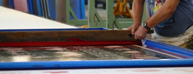 Artisan appliquant une encre rouge sur textile avec un cadre d’impression à la main