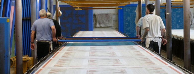 Artisans manipulant un cadre d’impression sur une grande table textile en atelier