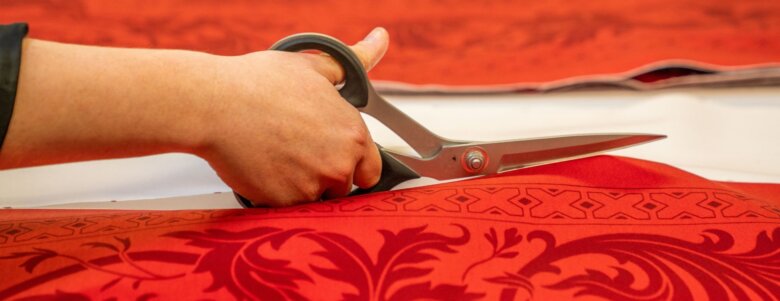 Main découpant un tissu rouge imprimé avec des ciseaux dans un atelier textile