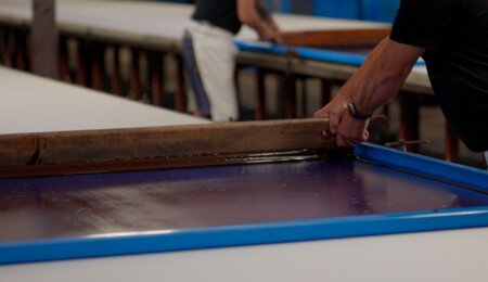 Artisan manipulant un cadre d’impression avec encre sur une table textile