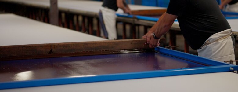 Artisan manipulant un cadre d’impression avec encre sur une table textile