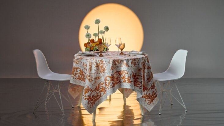 Nappe Beauvillé Topkapi coloris abricot sur une table ronde dressée avec verres et fruits, motif décoratif inspiré des palais orientaux dans des tons orange et crème.